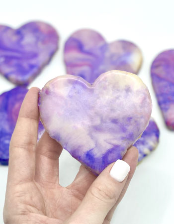 A woman holding a violet sugar cookie in her hand